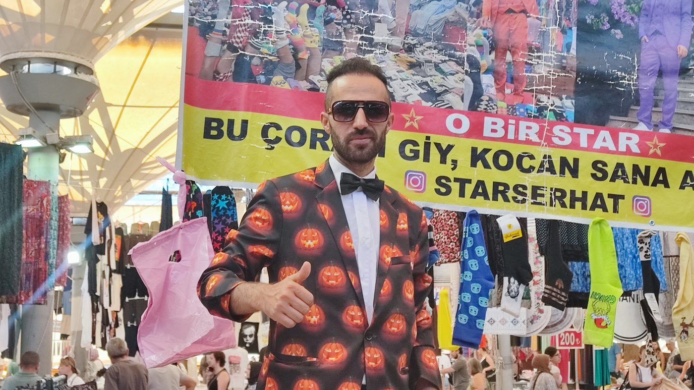 Salı Pazarı'nın simalarından Star Serhat, tezgâhının önünde papyonu ve desenli takımıyla